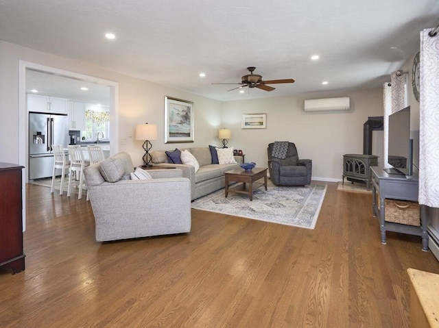 living room featuring recessed lighting, a wood stove, wood finished floors, a wall mounted AC, and a ceiling fan