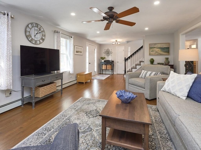 living area featuring stairs, baseboard heating, recessed lighting, wood finished floors, and a ceiling fan