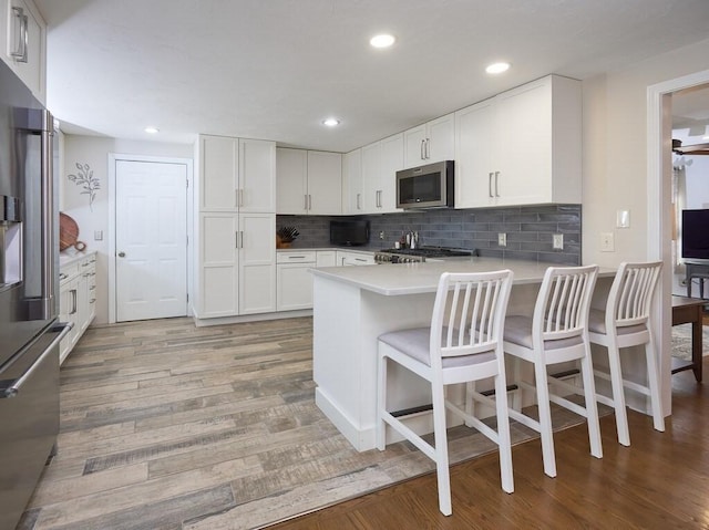 kitchen with light wood-style flooring, stainless steel appliances, a peninsula, white cabinets, and decorative backsplash