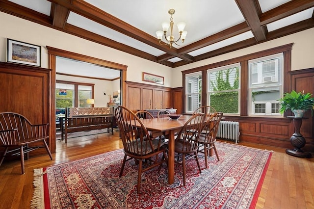 dining area featuring coffered ceiling, a chandelier, beam ceiling, radiator, and wainscoting