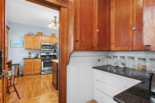 kitchen featuring stainless steel appliances, light wood finished floors, dark stone countertops, and a chandelier