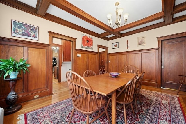 dining room featuring coffered ceiling, a chandelier, beamed ceiling, wainscoting, and light wood-style floors