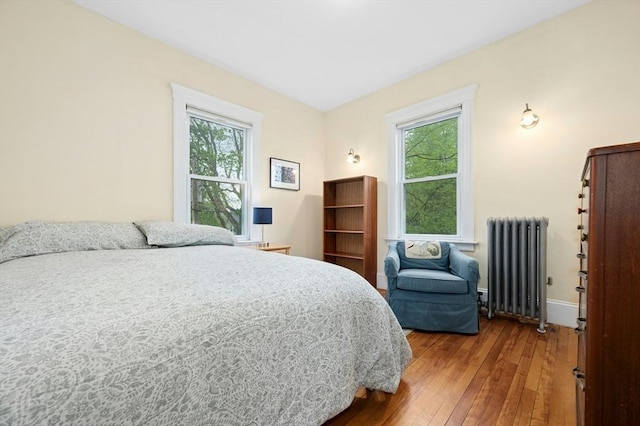 bedroom featuring radiator, wood-type flooring, multiple windows, and baseboards
