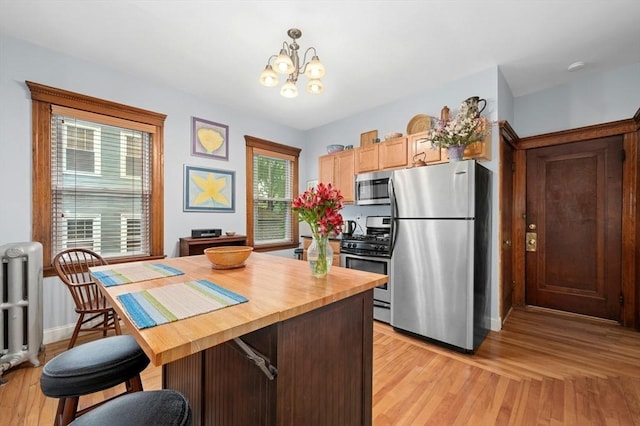 kitchen with appliances with stainless steel finishes, butcher block countertops, a chandelier, radiator heating unit, and light wood-style floors