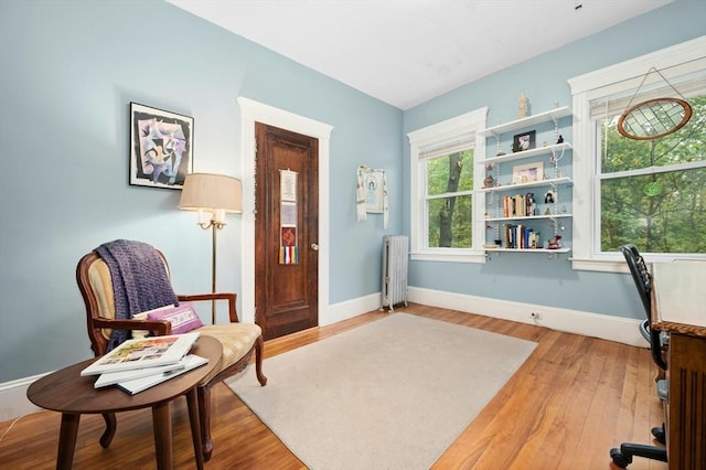 living area featuring radiator heating unit, baseboards, and light wood finished floors
