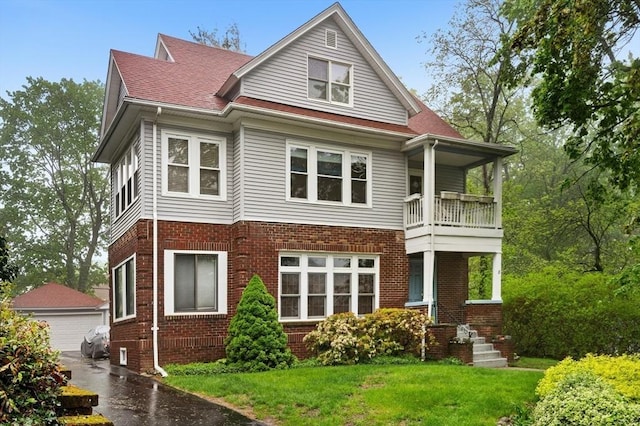 rear view of property with a balcony, brick siding, an outbuilding, a yard, and a detached garage