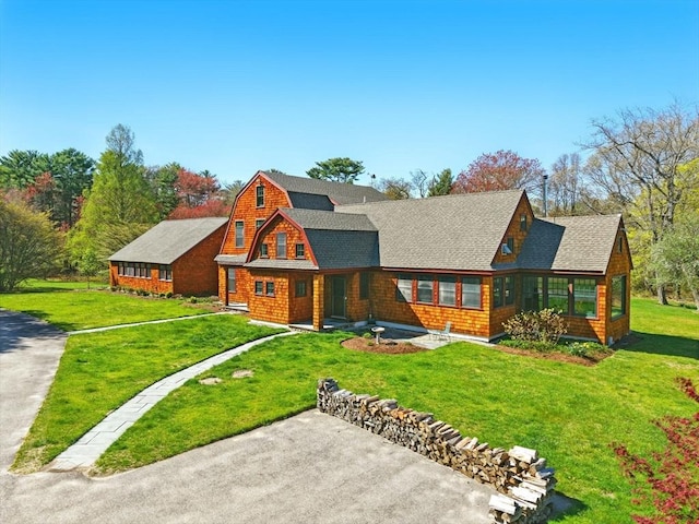 rear view of property featuring a yard, driveway, roof with shingles, and a gambrel roof