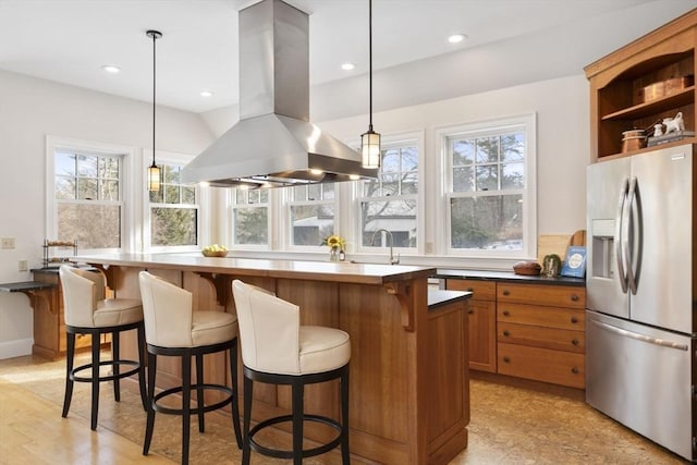 kitchen featuring brown cabinets, dark countertops, stainless steel fridge, island exhaust hood, and pendant lighting