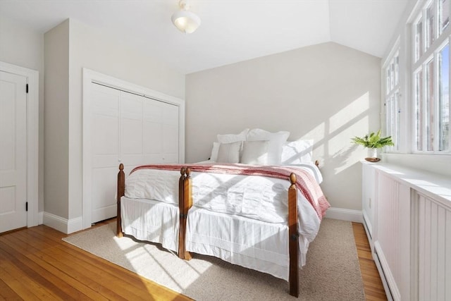 bedroom featuring baseboard heating, vaulted ceiling, light wood-type flooring, baseboards, and a closet