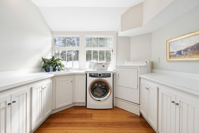 laundry area with light wood-type flooring, cabinet space, and washing machine and clothes dryer