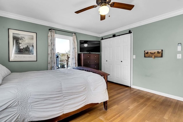 bedroom with wood finished floors, a barn door, crown molding, baseboards, and ceiling fan