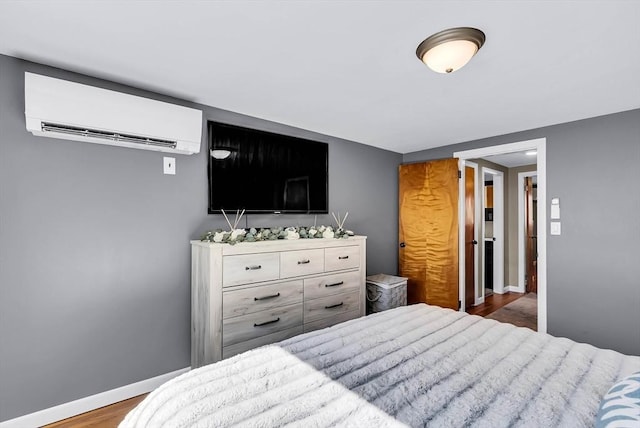 bedroom featuring a wall mounted air conditioner, baseboards, and wood finished floors