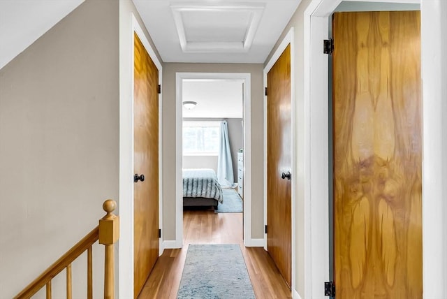 corridor featuring light wood finished floors, attic access, and baseboards