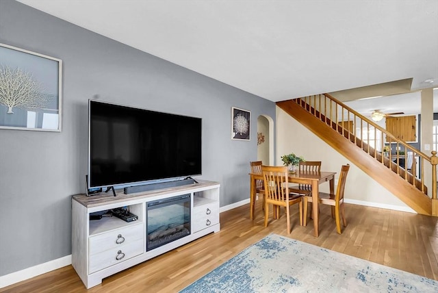 living area featuring arched walkways, stairs, baseboards, and wood finished floors