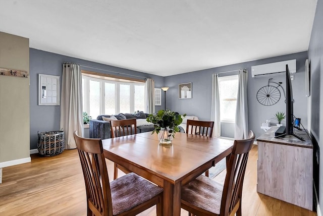 dining area with a wall mounted air conditioner, baseboards, and light wood-style floors