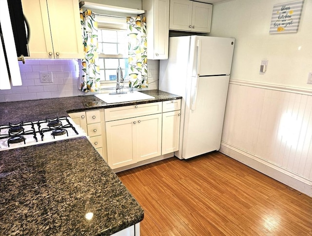 kitchen with sink, light hardwood / wood-style flooring, dark stone countertops, white cabinets, and white fridge