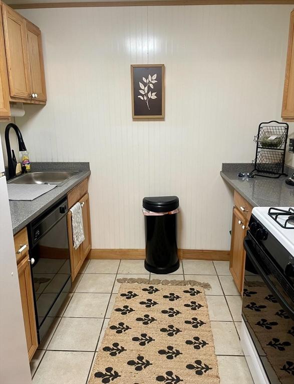 kitchen with light tile patterned floors, dishwasher, dark countertops, and a sink