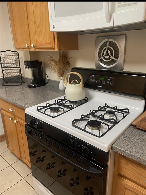 kitchen featuring brown cabinetry, light tile patterned floors, and white appliances