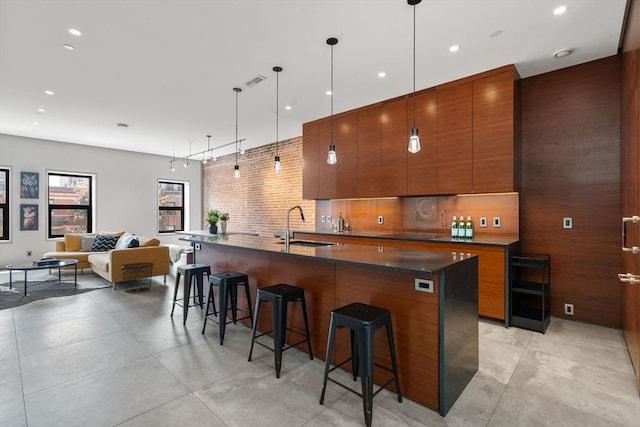 kitchen featuring modern cabinets, a breakfast bar, brown cabinets, a sink, and a center island with sink