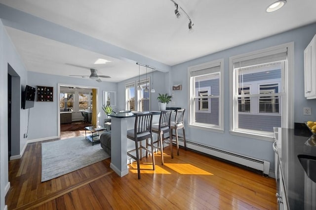 bar with track lighting, a baseboard radiator, wood-type flooring, and baseboards