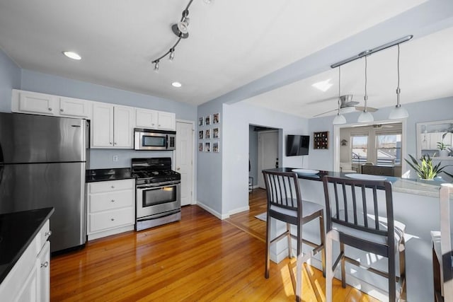 kitchen with stainless steel appliances, light wood finished floors, dark countertops, and white cabinetry