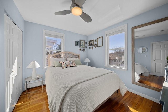 bedroom with baseboards, a baseboard radiator, ceiling fan, wood finished floors, and a closet