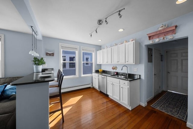 kitchen with dark countertops, stainless steel dishwasher, a baseboard heating unit, white cabinetry, and a sink