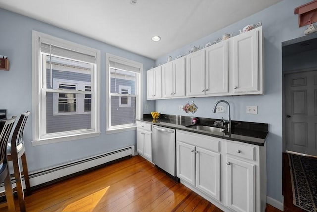 kitchen featuring dark countertops, wood-type flooring, baseboard heating, stainless steel dishwasher, and a sink