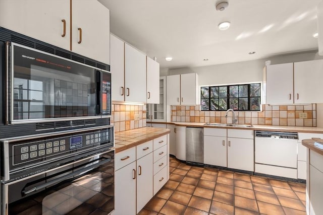 kitchen with decorative backsplash, a sink, white cabinets, black appliances, and tile counters