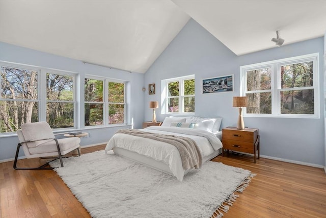 bedroom with baseboards, light wood finished floors, and high vaulted ceiling