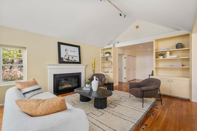 living area featuring a fireplace with flush hearth, track lighting, wood finished floors, and vaulted ceiling