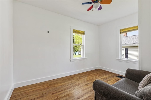 living area with baseboards, a ceiling fan, wood finished floors, and visible vents