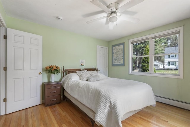 bedroom featuring light wood-style floors, ceiling fan, and a baseboard heating unit