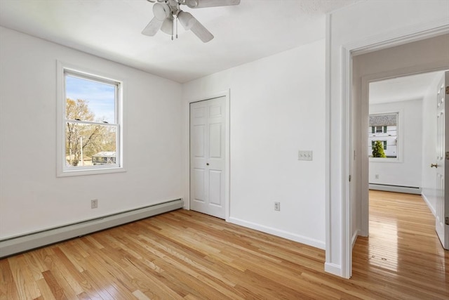 unfurnished bedroom featuring a baseboard radiator, a baseboard heating unit, light wood finished floors, and multiple windows