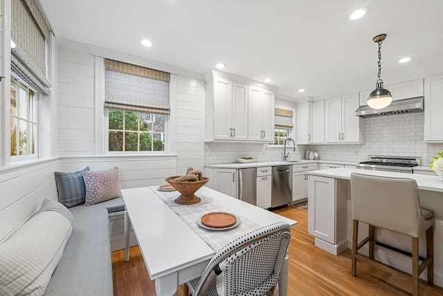 kitchen featuring hanging light fixtures, wall chimney range hood, white cabinets, and appliances with stainless steel finishes