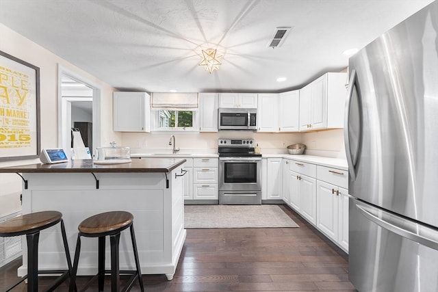 117 Woodland Dr, Lunenburg, MA 01462 - kitchen with stainless steel appliances, a breakfast bar, dark wood-style flooring, white cabinetry, and recessed lighting