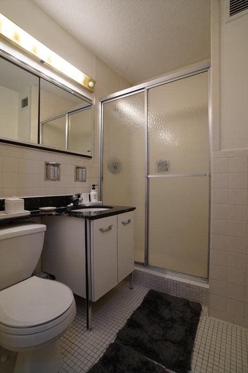 bathroom with tile patterned flooring, a textured ceiling, a shower with door, vanity, and tile walls