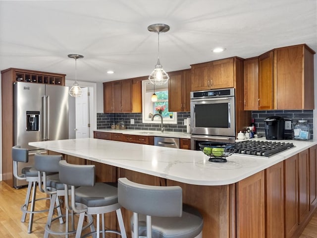886 Methuen St, Dracut, MA 01826 - kitchen featuring appliances with stainless steel finishes, brown cabinets, decorative backsplash, light wood-style flooring, and decorative light fixtures