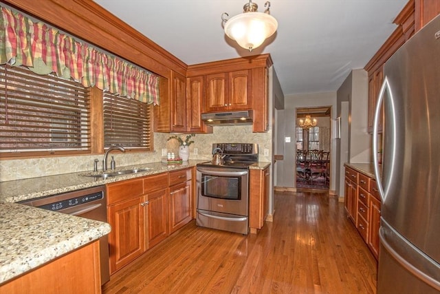 kitchen with backsplash, light hardwood / wood-style floors, pendant lighting, sink, and stainless steel appliances