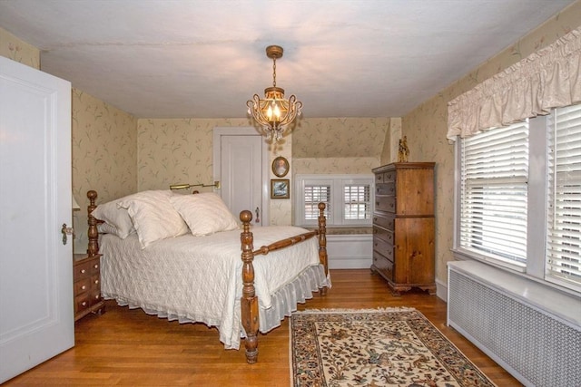 bedroom with radiator, an inviting chandelier, and wood-type flooring