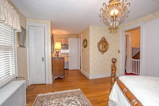 bedroom with a notable chandelier, radiator heating unit, multiple windows, and light hardwood / wood-style flooring