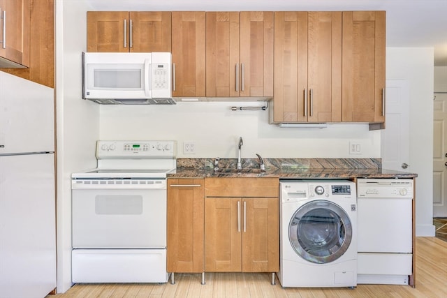 kitchen with light wood-type flooring, sink, white appliances, washer / dryer, and dark stone counters