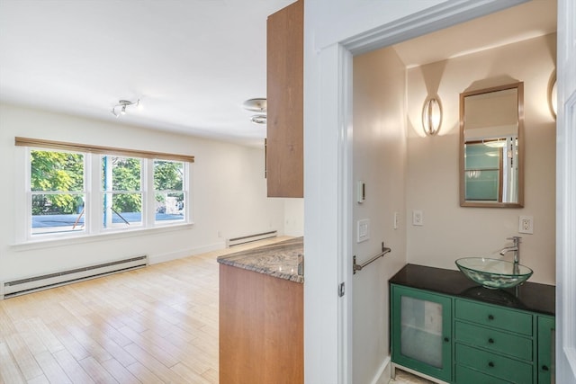 hall with light wood-type flooring, baseboard heating, and sink