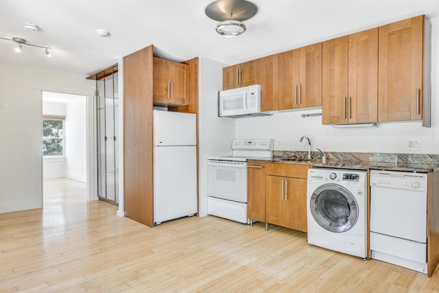 kitchen featuring washer / clothes dryer, white appliances, light hardwood / wood-style flooring, dark stone counters, and sink