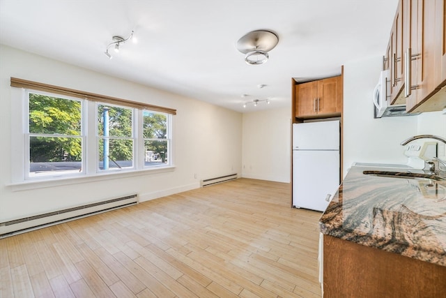 kitchen featuring dark stone countertops, a baseboard radiator, light wood-type flooring, and white appliances