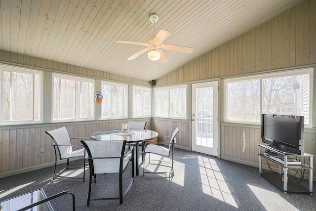 sunroom featuring outdoor dining area, a ceiling fan, plenty of natural light, and wooden walls