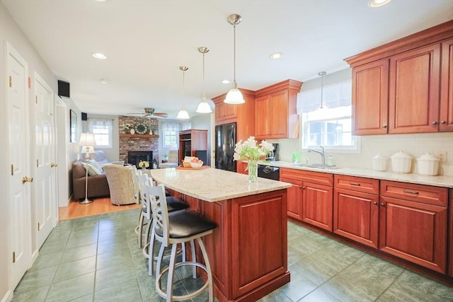 kitchen with a brick fireplace, a sink, light tile patterned floors, black appliances, and a breakfast bar