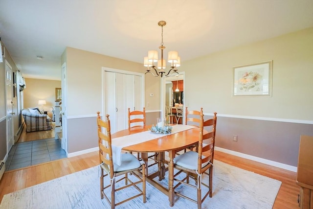 dining space with a baseboard heating unit, baseboards, a notable chandelier, and light wood-style flooring