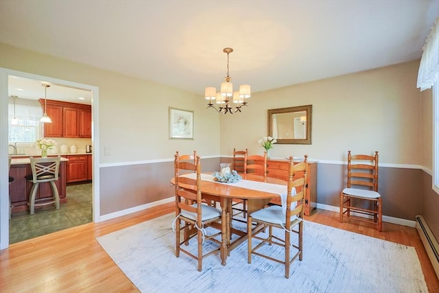 dining area with a chandelier, baseboards, a baseboard heating unit, and light wood-style flooring