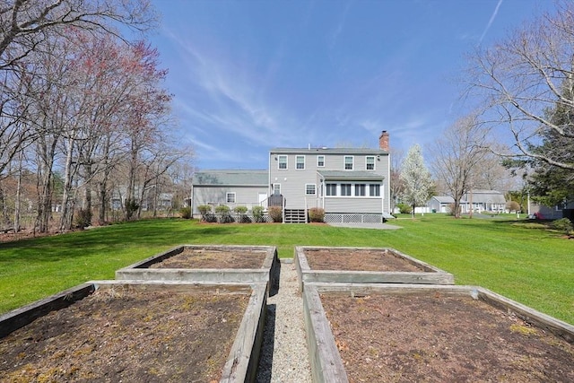 back of house with a lawn, a garden, and a chimney